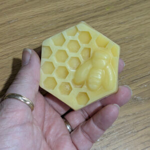 Hand holding an hexagonal beeswax block with honeycomb and bee design