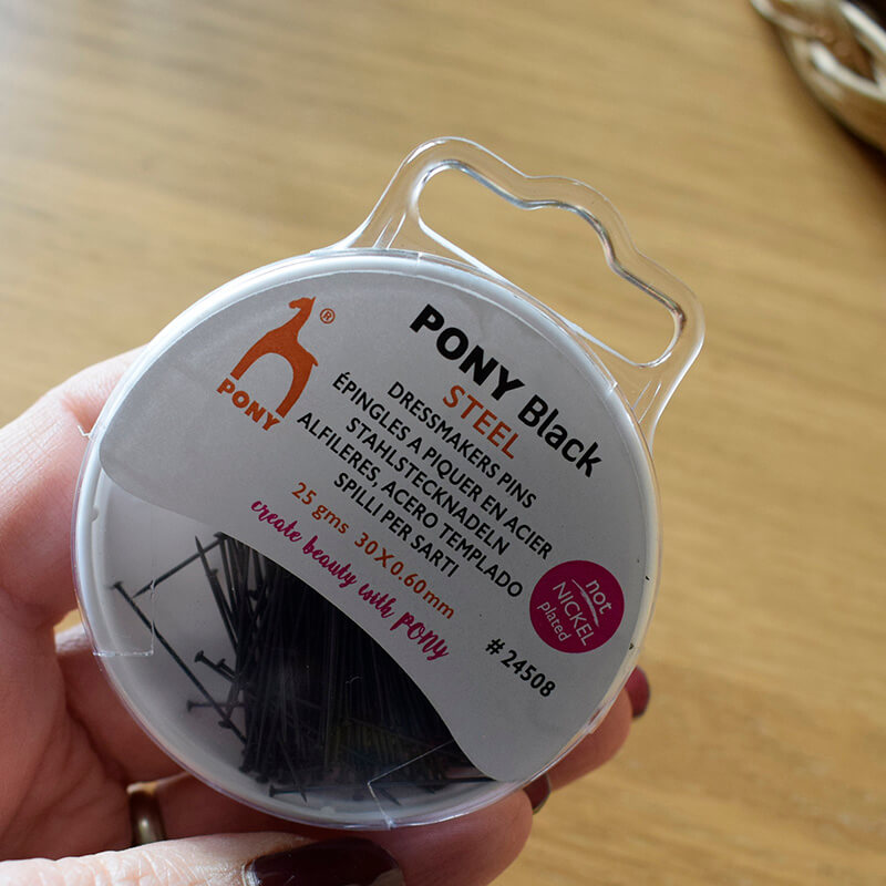 Hand holding a box filled with black coloured dressmaker pins