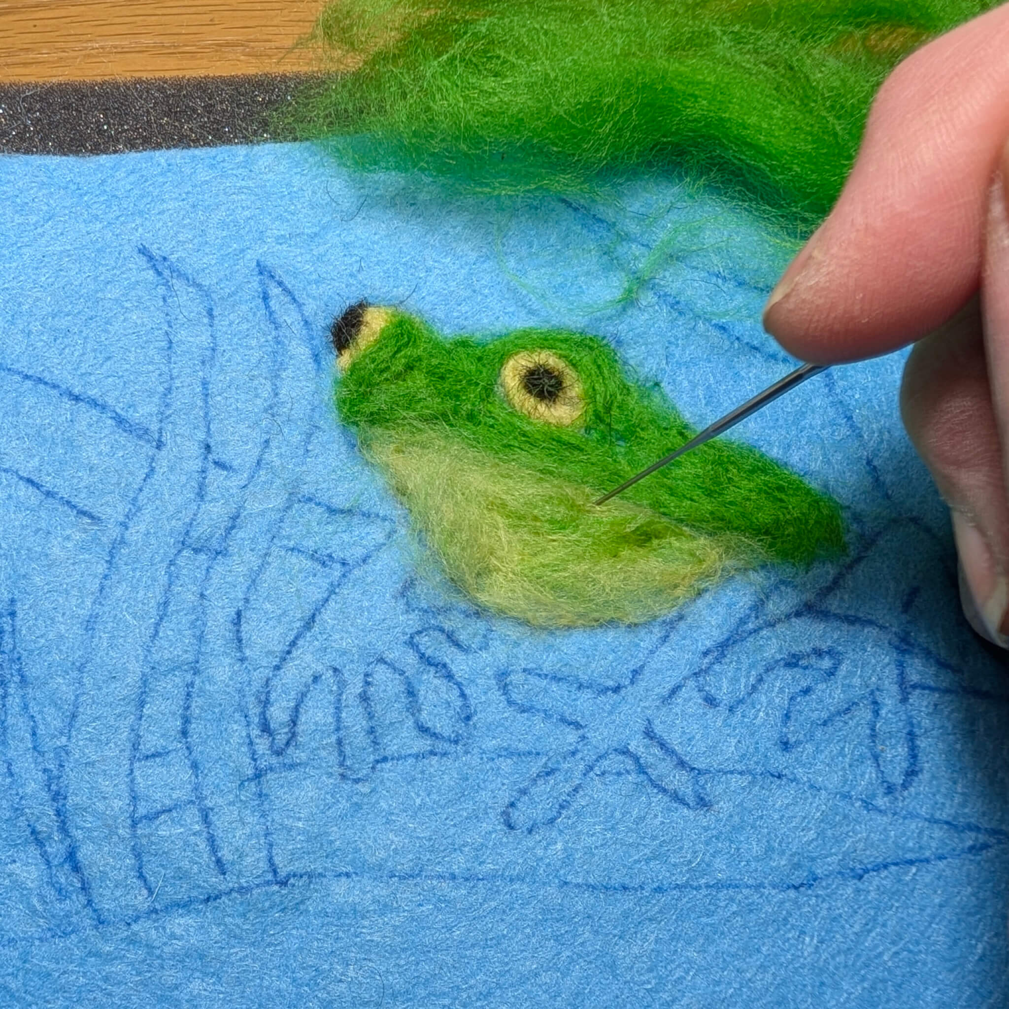 picture of a frog outline on a piece of felt with a hand stabbing some coloured felt within the outline
